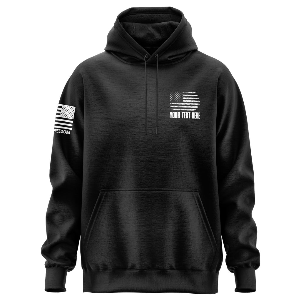 A black pullover hoodie with a white distressed American flag graphic on the left chest and 'YOUR TEXT HERE' underneath, plus a matching flag graphic on the right sleeve with 'FREEDOM' text. The hoodie is shown on a plain white background.